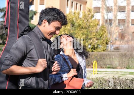 Latin friends laughing at the college campus with a guitar case. University life. Stock Photo