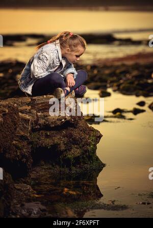 Girl sitting on a coastal rock looking into ocean, Ireland Stock Photo