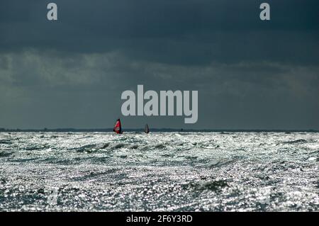 Dramatic lighting and glistening waves: two lonely sail boarders on the horizon near Thiessow beach on Rügen island, a popular area for windsurfing and kitesurfing. Stock Photo