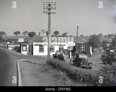 1957, historical, exterior view of the famous 'Horse Shoe Marriage Room', and Ye Old Toll Bar in Gretna Green, Scotland, established as the sign on the single-storey building says, in 1830 with over 10,000 marriages performed there. Motor cars of the era are parked in the car park, as well as a motobike and sidecar.  At this time, the entrance to the marriage room was through 'Ye Old Toll Bar', where souvenirs and postcards were sold. The Old Toll Bar at Gretna, part of its run-away wedding legacy, was known as the First House in Scotland, as written on the side of the old cottage. Stock Photo