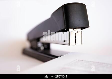 Close-up front view of a black stapler stapling several sheets of paper together. On white background Stock Photo