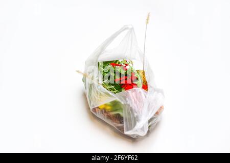 DEFOCUS. Environmental pollution. Red and green plants flowers in a plastic bag on a white background. A dry blade of grass sticks out. Ecological pro Stock Photo
