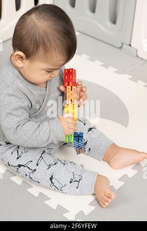 Six month old baby boy sitting, holding and inspecting colorful wooden toy, moving it from one hand to the other Stock Photo