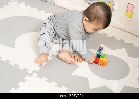 Six month old baby boy sitting leaning over to pick up toy Stock Photo