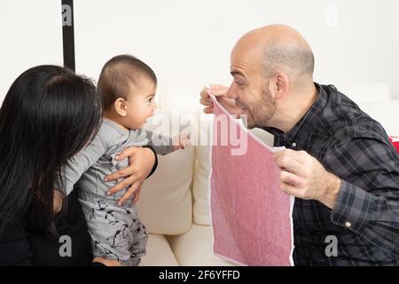 Six month old baby boy peek a boo game with father and mother Stock Photo