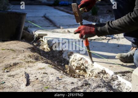 Defocus bricklayer removing irregularities on floor screed with hammer and chisel. Male hands in red work gloves hold a hammer and chisel. Out of focu Stock Photo