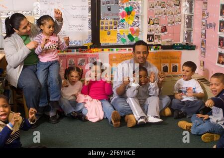 Preschool classroom 4 year olds female teacher and male student teacher with group at cicrle time singing song with hand gestures Stock Photo