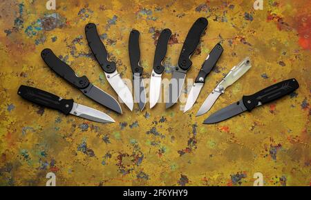A variety of folding and pocket knives on a yellow old metal background. Stock Photo