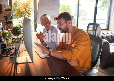 Young focused businessman being mentored by senior female partner in the office Stock Photo