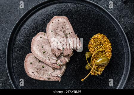 Pork boiled tongue slices on a plate. Black background. Top view Stock Photo