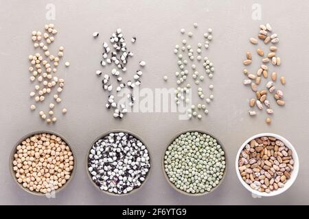 Different types of legumes in bowls and scattered in the background, green peas and Pinto beans, chickpeas and beans, top view Stock Photo