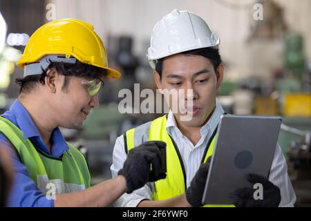 Two workers in production plant as team discussing, industrial scene in background, working together manufacturing activities Stock Photo