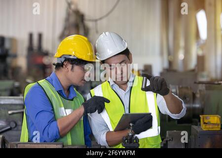 Two workers in production plant as team discussing, industrial scene in background, working together manufacturing activities Stock Photo