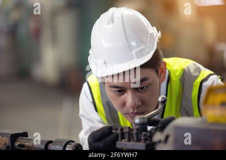 A worker in glasses standing near industrial equipment and verifies production. man operating machine in the factory Stock Photo