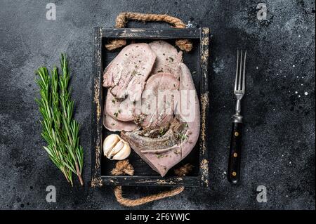 Cooked Boiled veal or beef tongue sliced in a wooden tray. Black background. Top view Stock Photo