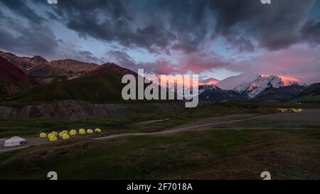 Idyllic purple-red sunset in the base camp of Lenin Peak, Pamir mountains with climbing tents and yurt Stock Photo