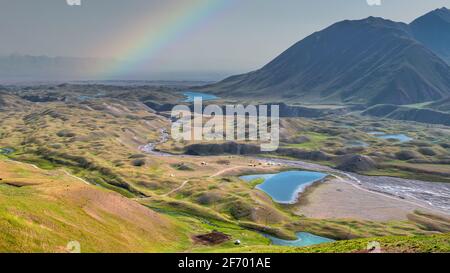 Colourful rainbow soaring over blue glacier lagoons and mountain hills of Pamir mountain range on the border of Kyrgyzstan and Tajikistan Central Asia Stock Photo