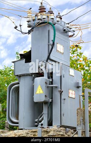 An old transformer substation for the distribution of electricity stands in the middle of a summer garden against a blue cloudy sky. Vertical image. Stock Photo