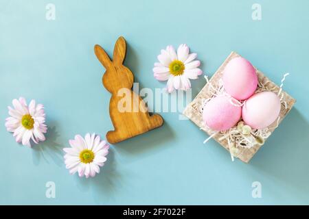 Minimal spring Easter concept. Paper box with Easter eggs in pink tones and chrysanthemums flower on pastel blue background. Top view flat lay. Stock Photo