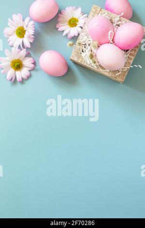Minimal spring Easter concept. Paper box with Easter eggs in pink tones and chrysanthemums flower on pastel blue background. Top view flat lay. Copy s Stock Photo