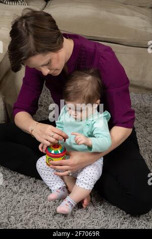 10 month old baby girl with mother, shown how musical toy with crank works Stock Photo