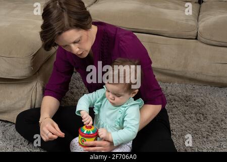 10 month old baby girl with mother, trying to turn crank on musical toy after being shown how it works Stock Photo