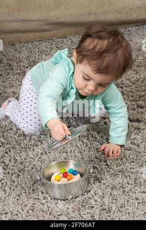 10 month old baby girl opening lid on pot to find hidden toy Piaget object permanence Stock Photo