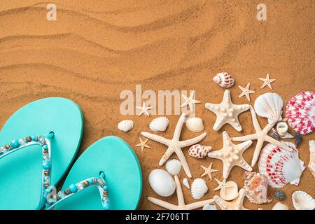 Blue flip-flops and starfish and seashells on the sand. Top view with copy space. Stock Photo