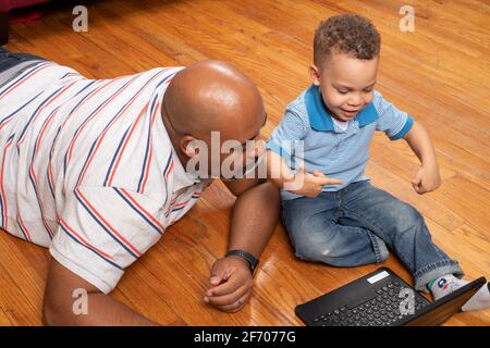 3 year old boy at home with father home learning using ipad provided by school district for at home learning during Covid-19 pandemic Stock Photo