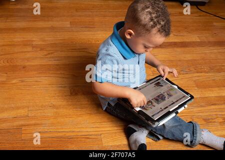 3 year old boy sitting on floor using tablet device supplied by PreK program for home use during Covid-19 pandemic shutdown Stock Photo
