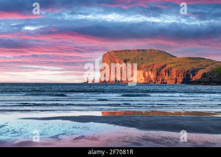 Incredible sunset in low tide time on Atlantic ocean coast near village Tjornuvik. Famous rock formations Risin and Kellingin Eidiskollur on backgroun Stock Photo