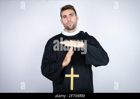 Young hispanic man wearing priest uniform standing over white background Doing time out gesture with hands, frustrated and serious face Stock Photo