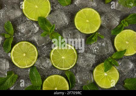 Close up flat lay of lime slices, fresh green mint leaves and ice cubes on grunge gray stone table surface, elevated top view, directly above Stock Photo
