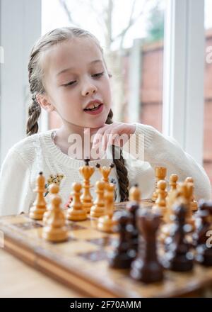 Beautiful cute genius child young girl playing chess with pieces on chessboard kid concentrating player on king queen for checkmate Stock Photo
