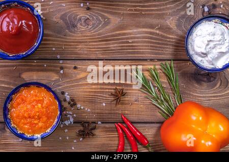 Sauce in the assortment on a brown wooden background, decorated with pepper, cherry tomatoes, spices, coarse salt. Restaurant menu. Stock Photo
