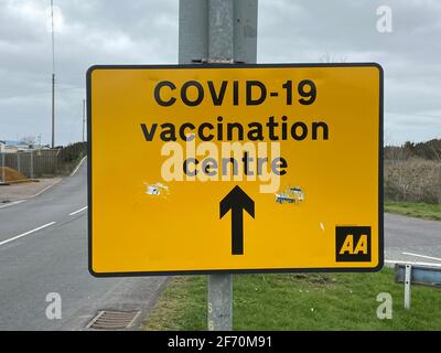 Covid-19 vaccination Centre, New Romney, East Sussex, UK - 03.03.2021: Yellow road sign directing to  Covid-19 Vaccination centre. Stock Photo