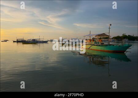 Boat with outriggers moored off Logon, Malapascua Island at dusk. Visayan Sea, Cebu, Philippines. Stock Photo