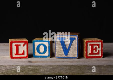"Love" spelled in vintage wooden blocks on old wood and black background. Stock Photo