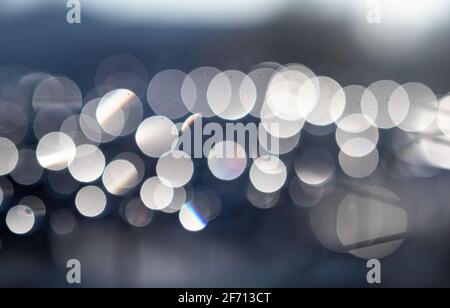 Bokeh lights from water drops on mesh outside early mornings. Defocused and abstract dapples of white arranged in a horizontal line. Stock Photo