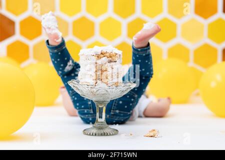 A toddler's feet smeared in cream, and a cake on a plate close up. The child is lying on the floor. In the background is a pattern of yellow honeycomb Stock Photo