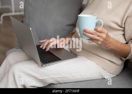 Mature woman using laptop at home, sitting on couch Stock Photo