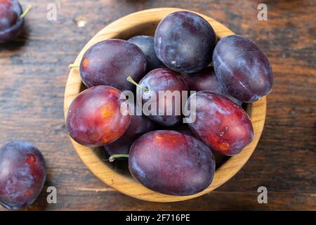 Fresh plums in a wooden bowl on a brown table. Gathering the summer harvest. Stock Photo