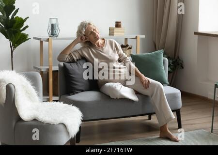 Serene mature 60s woman relaxing in modern comfortable living room Stock Photo