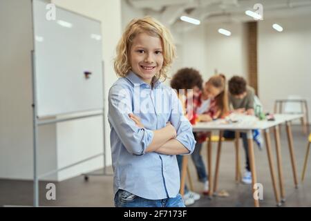 Smart guy. Portrait of joyful boy smiling at camera, standing with arms crossed while posing for camera during crafting classes. Kids working on diy Stock Photo