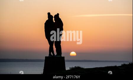 Bournemouth, UK. 4th April 2021.  A couple enjoy the moment as the sun rises on Easter Day at Hengistbury Head in Bournemouth, Dorset at the start of a bright and sunny day along the south coast. Credit: Richard Crease/Alamy Live News Stock Photo