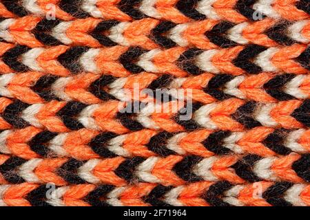 Synthetic knitted fabric with pattern elements of red, black and white yarns close up. Multicolor patterned knitted fabric texture. Background Stock Photo