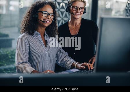 Two businesswomen looking at computer screen and smiling. Mature business colleagues working together in the call center. Stock Photo