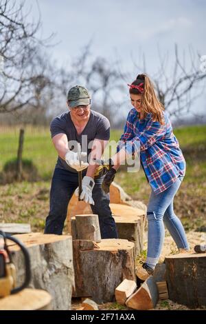 Husband teaching his strong wife how to split logs with the heavy axe Stock Photo