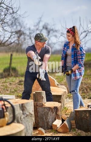 Husband teaching his strong wife how to split logs with the heavy axe Stock Photo