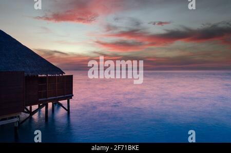 water villa silhouette with a purple sunset over the ocean. Stock Photo